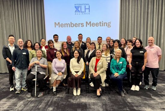 29 smiling people are gathered in three rows beneath the International XLH Alliance logo.